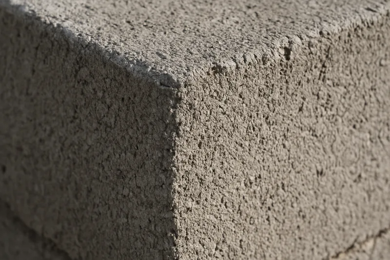 The square corner of a single concrete block lit from the side so its rough texture shows — block wall, Idaho Falls. Illustrative example.