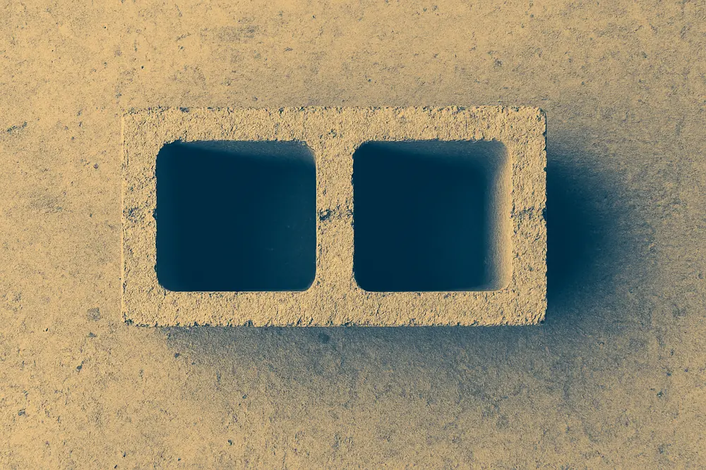 A single hollow concrete block with two open cores seen from directly above on a bare concrete floor — block wall, Idaho Falls. Illustrative example.